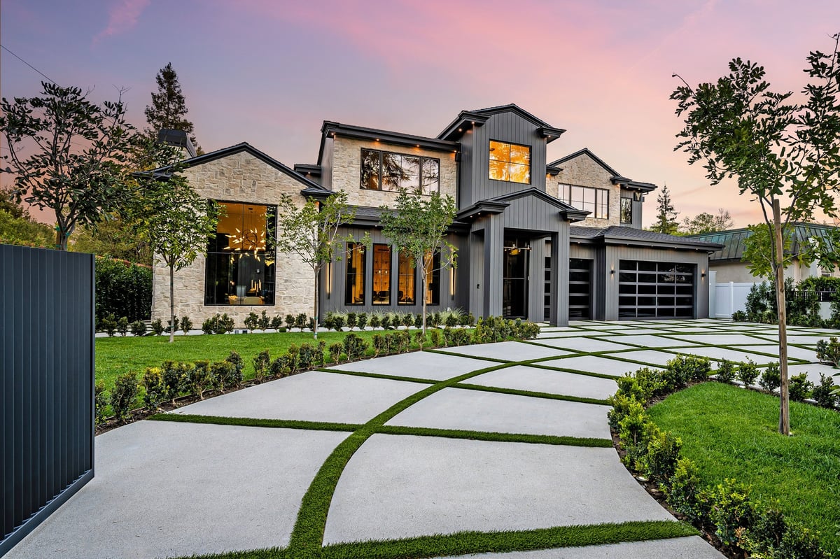 Modern luxury home exterior with a well-manicured lawn, geometric driveway, and sunset sky